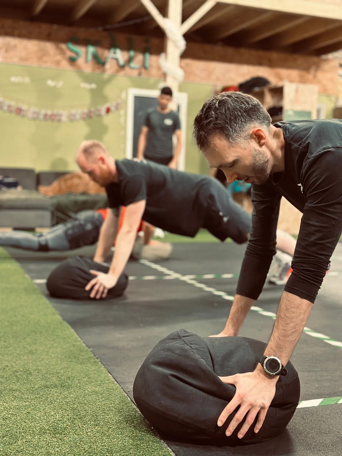 Gainage sur sandbag pendant un cours de CrossTraining, le coach à côté